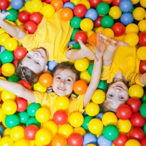 Three happy little kids girls in ball pit smiling happily at camera while having fun in children play center. Top view